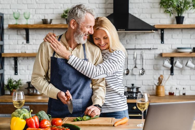 woman gives her husband a hug while he cooks in the kitchen